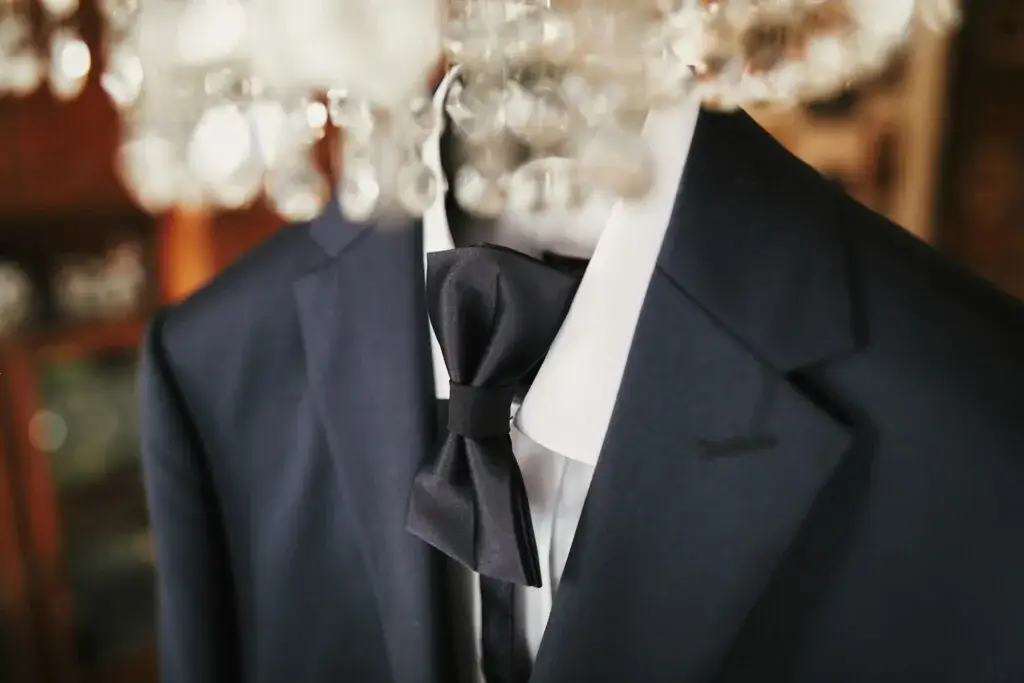 stylish black suit with white shirt and bow tie on hanger on luxury chandelier